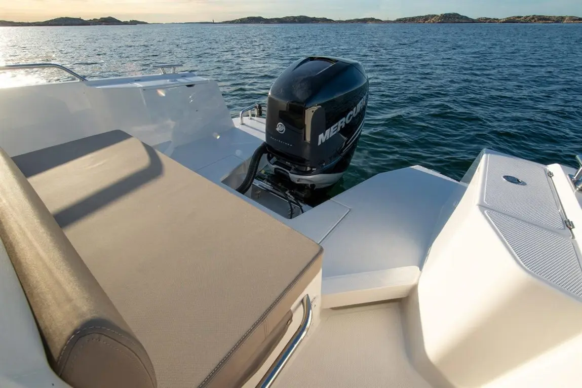 A luxury boat's deck with a Mercury outboard motor on the water, featuring a sunbathing area and scenic coastline in the background.